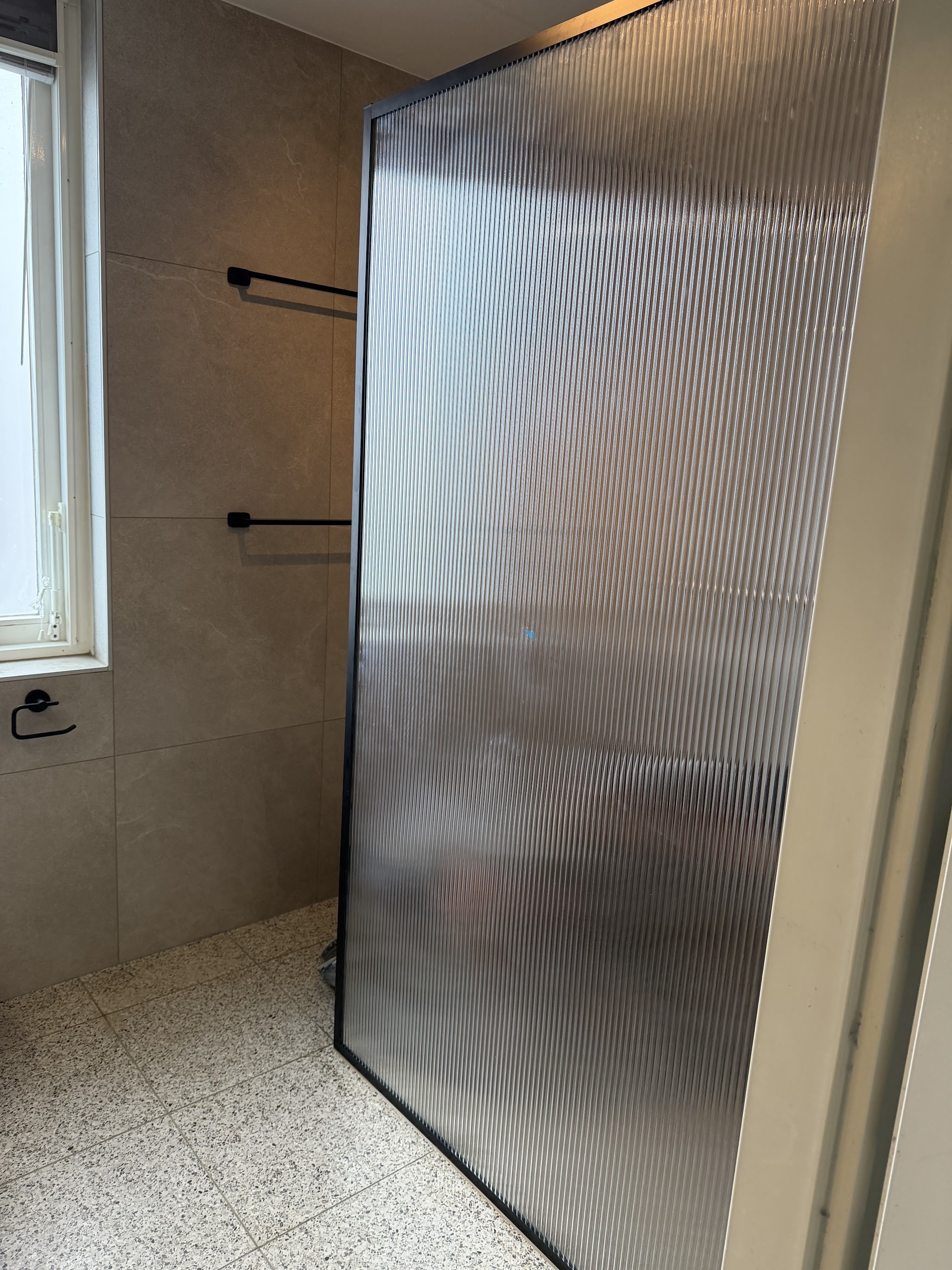 Douche met geribbelde glazen wand en terrazzo vloer