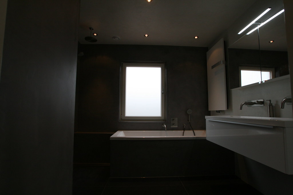 Donkere badkamer met ligbad en wastafelmeubel onder het raam