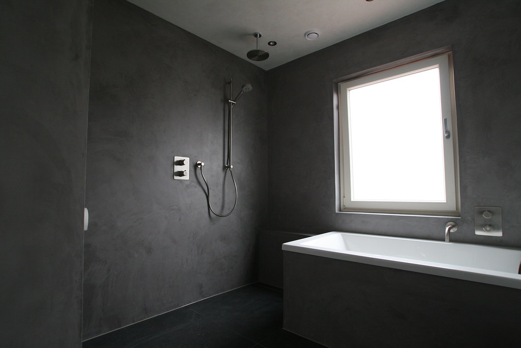 Badkamer in betonlook met ligbad onder het raam