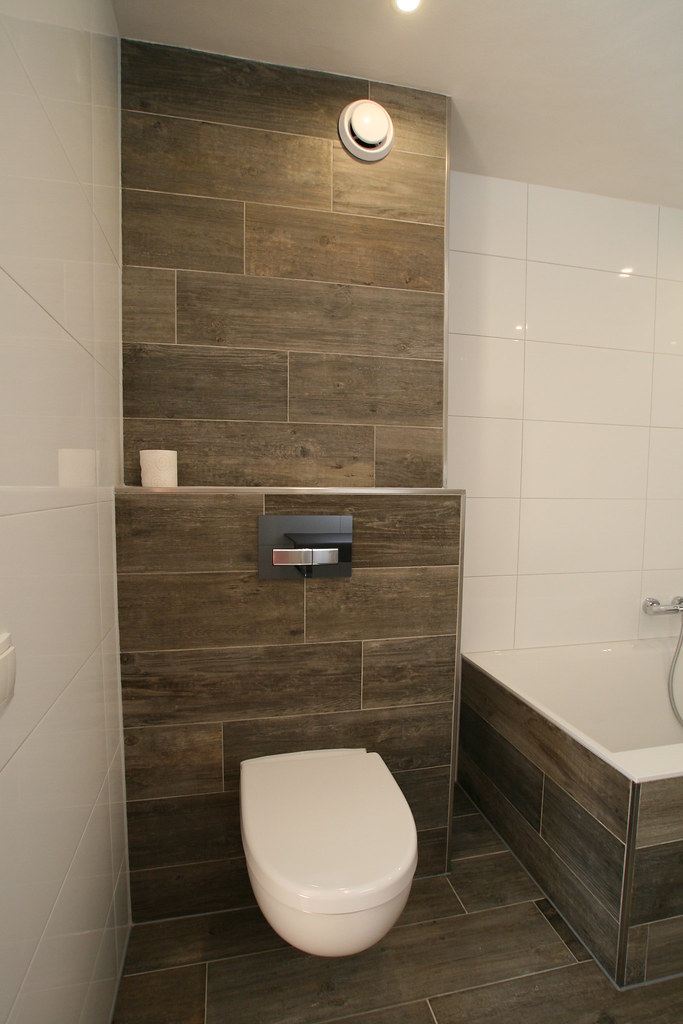 Witte tegels met een donkere houtlook wand en ligbad